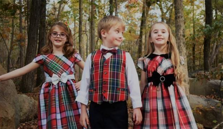 Three children in plaid outfits in a forest